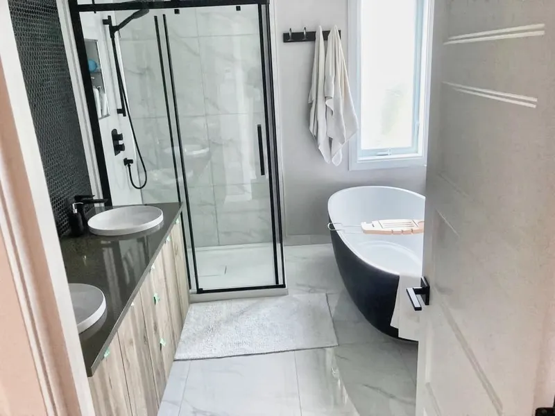 Salle de bain contemporaine — baignoire autoportante noire, douche vitrée et céramique marbrée
